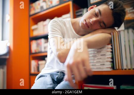 Männlicher Student, der in der Bibliothek schläft. Studieren, Hausaufgaben machen. Stockfoto