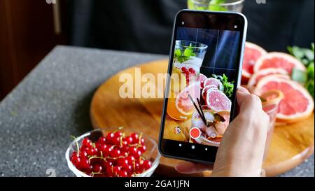 Eine Frau fotografiert am Telefon Grapefruitlimonade. Flach legen ein erfrischendes kaltes Getränk im Sommer Stockfoto