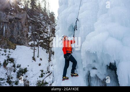 Luftaufnahme eines gefrorenen Wasserfalls und Felsen, bei dem Kletterer seine eisbedeckte Oberfläche mit Eispickeln und Steigeisen aufsteigen Stockfoto