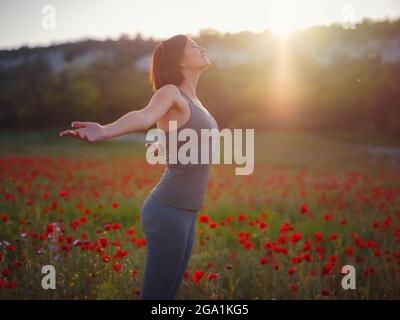 Junge schöne Frau mit erhobenen Armen im Frühjahr Mohnfeld. Sanfte Farben. Nachdenkliche, entspannte Atmosphäre. Stockfoto