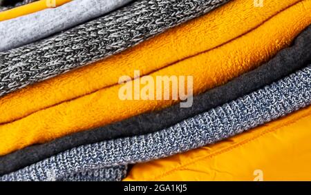 Haufen der grauen und gelben warmen Strickpullover und Pullover aus nächster Nähe. Natürlicher textiler Hintergrund. Stockfoto