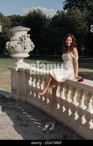 Neben einer Statue steht eine junge schöne Dame in weißem Kleid mit roter Rose Stockfoto