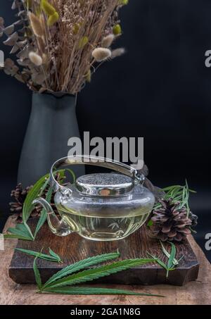 Cannabis Kräutertee aus Teekannen und Stiel mit grünen Marihuanablättern auf Holzhintergrund. Medizinische Zwecke für Schlaf und Angst. Kräutertee und Gesundheit Stockfoto