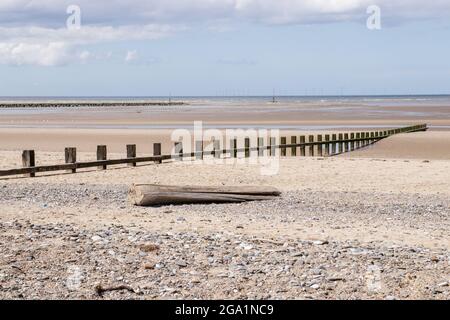 Rhyl North Wales, Blick auf das Meer, Sand und Stein, Treibholz, Rillen, die zum Meer führen, blauer Himmel mit weißen, flauschigen Wolken Stockfoto