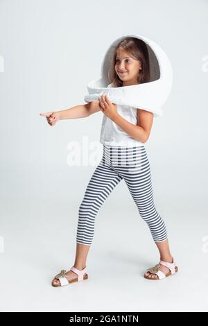 In voller Länge Porträt der schönen Vorschule Mädchen in großen weißen Astronaut Helm isoliert auf grauen Studio-Hintergrund. Kindheit, Bildung, Emotion Stockfoto