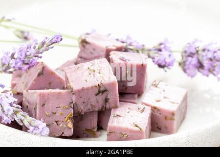 Lavendelkäse mit trockenen Lavendelblüten auf weißem Teller serviert. Würfel von purpurem Käse mit pflanzlichen Zutaten Stockfoto