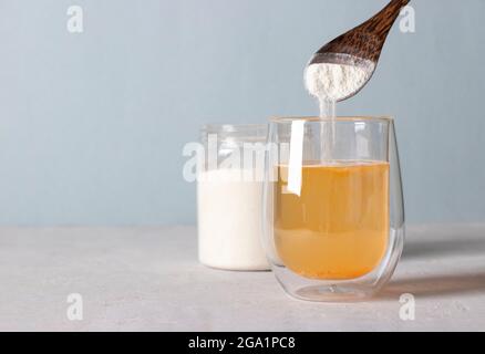 Kollagenpulver wird mit einem Löffel in ein Glas Wasser gegeben. Gesundes Anti-Age-Konzept auf hellblauem Hintergrund. Platz für Text Stockfoto