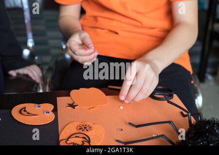 Halloween Kinder Handwerk Vorbereitungen. Kleine Kinder, die zu Hause oder in der Schule basteln, tragen orangefarbene und schwarze Kleidung Stockfoto