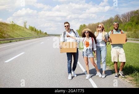 Gruppe multiethnischer Freunde mit leeren Schildern, die auf der Straße herumhiksten, eine Fahrt fangen, mit einem Autostop fahren, Platz kopieren Stockfoto