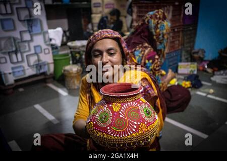 Dharavi, Mumbai, Maharastra, Indien. Juli 2021. Eine Frau bei Dharavi gab den letzten Schliff auf einem irdenen Topf, bevor sie ihn auf den Markt schickte. Dharavi ist eine Ortschaft in Mumbai, Maharashtra, Indien, die als eines der größten Slums Asiens gilt. Dharavi hat eine Fläche von etwas mehr als 2.1 Quadratkilometern und eine Bevölkerung von etwa 1,000,000. Mit einer Bevölkerungsdichte von über 277,136/km2 (717,780/Quadratmeilen) ist Dharavi eines der am dichtesten besiedelten Gebiete der Welt.das Slum Dharavi wurde 1884 gegründet.Dharavi verfügt über eine dynamische informelle Wirtschaft, in der zahlreiche Haushaltsunternehmen viele der Slums beschäftigen Stockfoto