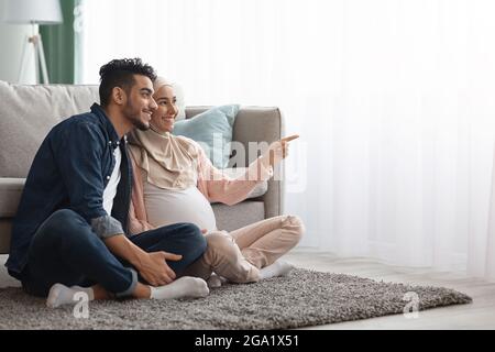 Porträt Eines Glücklichen Schwangeren Paar Aus Dem Nahen Osten, Das Sich Auf Dem Boden Ausruht Wohnzimmer Stockfoto