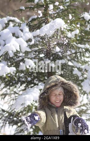 Kleines Mädchen, das im schneebedeckten Winterwald spazierengeht. Kinderfreude im Schnee, der von den Zweigen einer Fichte fällt. Stockfoto