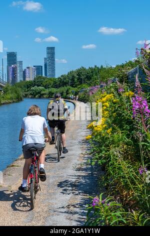 Mann und Frau radeln auf dem Abschleppweg des bridgewater Kanals zum stadtzentrum von manchester entlang des Abschleppweges mit hohen Stadtgebäuden im hinteren Teil. Stockfoto