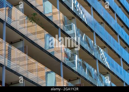 Das Muster besteht aus Balkonen in einem mehrstöckigen Wohnblock mit Glasfront, die andere Gebäude in einer Stadt- oder Straßenumgebung reflektiert. Stockfoto