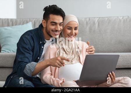 Fröhlich Schwanger Muslimische Frau Und Ihr Mann Mit Laptop An Gemeinsam Zu Hause Stockfoto