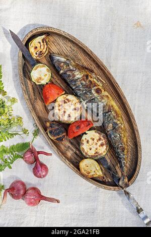 Köstlicher Gemüsekebab und Makrele. Gegrillter Meeresfisch und Gemüse auf einer Holzplatte. Gegrillter Fisch. Gebratener Fisch, gebackenes Gemüse und Sauce. Stockfoto