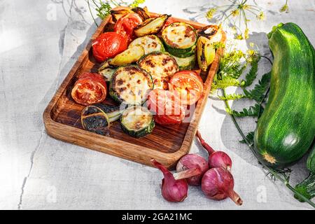 Gegrillte Zucchini, Tomaten und süße Zwiebeln auf einer Holzplatte. Gemüsekebab. Gegrilltes Bio-Gemüse. Gekochtes Gemüse und Sauce. Essen immer noch Stockfoto