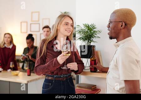 Glücklich junge Brünette Frau in rosa Pullover klinkende Flöte Champagner mit dem von ihrem Freund, während genießen Home Party Mit Freunden Stockfoto