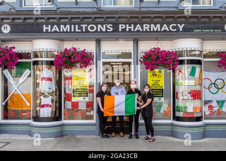 Skibbereen, West Cork, Irland. Juli 2021. Die Menschen in der Stadt Skibbereen bereiteten sich heute darauf vor, die irischen Ruderer zu unterstützen, die am morgigen Finale der Leichtgewicht-Doppelzweier-Sculls für Herren gegeneinander antreten. Die Ruderer Fintan McCarthy und Skibbereen's Paul O'Donovan holen sich um 1.50 Uhr Gold. Vor ihrem mit Olympia dekorierten Laden, Hamilton's Pharmacy, waren Stephanie Cronin, James Hamilton, Sharon Roycroft und Amy Minihane zu sehen. Quelle: AG News/Alamy Live News Stockfoto