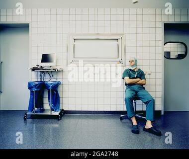 Chirurg sitzt in Peelings und OP-Kappe vor einem Operationssaal; Deutschland Stockfoto