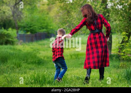 Mutter auf Spaziergang mit ihrem Sohn im Park. Frau und Kind in der Natur. Rückansicht. Familienlook. Rustikal. Der Elternteil hält die Hand des Kindes. Internationales Konzept für Familientag Stockfoto