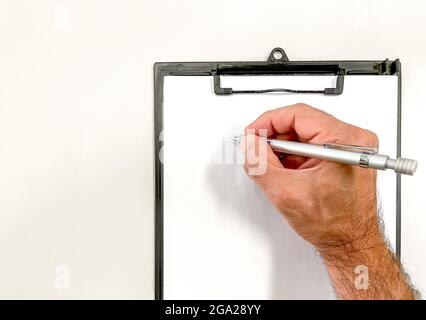 Hand mit einem Metallstift Schreiben auf einem leeren Blatt Papier auf einem Klemmbrett Ordner, Kopierraum, horizontal Stockfoto