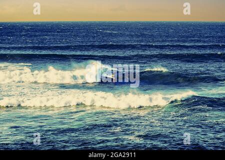 Im Ho'okipa Bach Park in der Nähe von Paia, mit einer blauen Meereslandschaft und einem orangenen Himmel, reitet ein einfarbigkeit Surfer auf den Wellen; Maui, Hawaii, USA Stockfoto