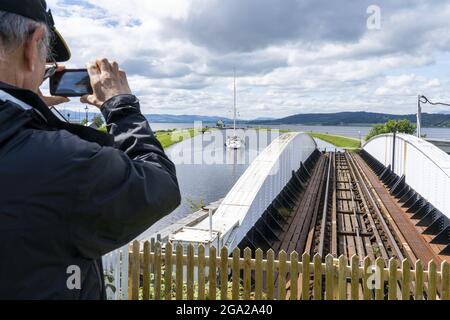 Ein Mann fotografiert die Schleuse, eine Segelboot- und Eisenbahnbrücke des Caledonian Canal in der Nähe von Inverness, Schottland; Inverness, Schottland Stockfoto