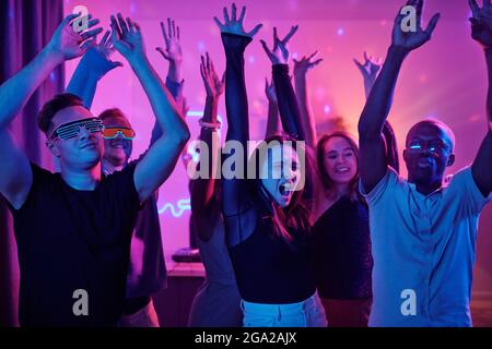 Glücklich junge glamouröse Frau der afrikanischen Ethnie in smart Kleid Schaut zur Seite, während ihr vor der Kamera tanzt Freunde zu Hause Party Stockfoto