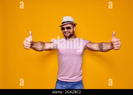 Bärtiger Mann mit Hut und Sonnenbrille zeigt Daumen nach oben Stockfoto