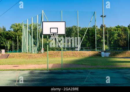 Basketballplatz in der Abendsonne. Ein weiteres Sprotrs-Feld (Fußballplatz) und einige Bäume im Hintergrund. Sommer, sonniger Tag. Stockfoto