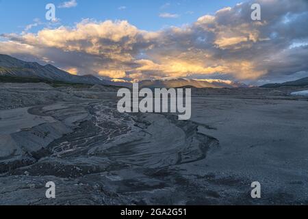 Die untergehende Sonne leuchtet die Wolken über den fernen Gipfeln des Kluane National Park, Yukon. Im Vordergrund fließt ein kleiner Strom. Das Hotel liegt im... Stockfoto