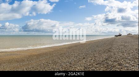 Blick auf die Küste entlang des Atlantiks am Kiesstrand von Dungeness an einem sonnigen Tag mit einem befahrenen Kabinenboot in der Ferne Stockfoto