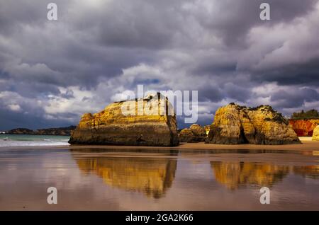 Dona Ana Strand bei Ebbe mit seiner felsigen Sandsteinküste und den Meeresstapeln entlang der berühmten Algarve Küste unter einem stürmischen Himmel Stockfoto