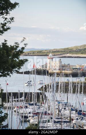 Segelboote dockten in der Marina im historischen Fischerdorf Howth an, wobei der Howth Lighthouse den Eingang zum Seehafen bewachte Stockfoto