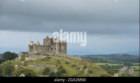 Der alte Rock of Cashel auf dem Hügel gegen einen bewölkten Himmel mit Hore Abbey und der Tipperary Landschaft unten; Cashel, County Tipperary, Irland Stockfoto