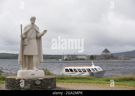 Statue von St. Patrick und Boot am Ufer des Lough Derg, mit der Pilgerstätte des St. Patrick's Fegefeuer auf Station Island im Hintergrund Stockfoto