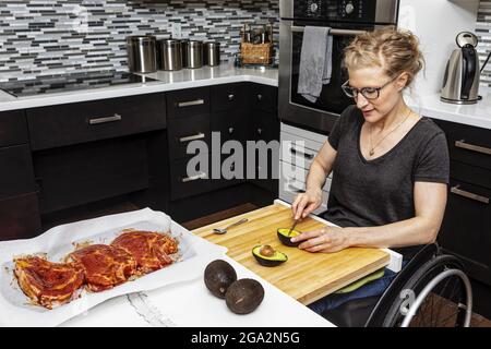 Eine querschnittsgelähmte Frau, die in ihrer Küche ein Essen für ihre Familie zubereitet, während sie von einem Rollstuhl aus arbeitet; Edmonton, Alberta, Kanada Stockfoto