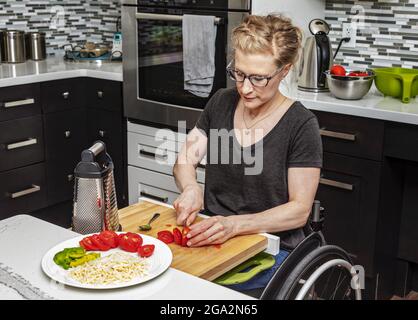 Eine querschnittsgelähmte Frau, die in ihrer Küche ein Essen für ihre Familie zubereitet, während sie von einem Rollstuhl aus arbeitet; Edmonton, Alberta, Kanada Stockfoto