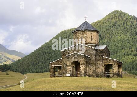 Alte Kirche der Heiligen Dreifaltigkeit in Shenako mit den bewaldeten Bergen des Großkaukasus im Hintergrund im Tusheti-Nationalpark Stockfoto