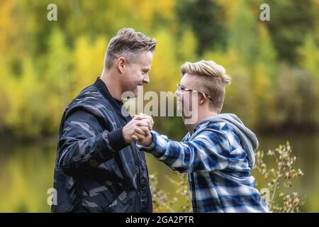 Ein junger Mann mit Down-Syndrom und sein Vater genießen die Gesellschaft des anderen und geben an einem warmen Herbstabend vor, in einem Stadtpark zu ringen Stockfoto