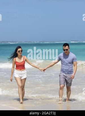 Ein Paar geht an einem weißen Sandstrand mit Händen entlang und genießt einen tropischen Urlaub entlang der Küste von Oahu, Hawaii Stockfoto