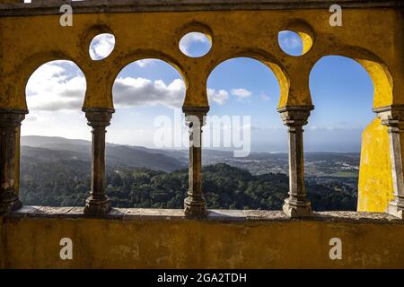 Blick durch die bunten Bögen und Säulen auf der Queen's Terrace mit Blick auf das bewaldete Gelände des Pena Parks und die Sintra Berge... Stockfoto