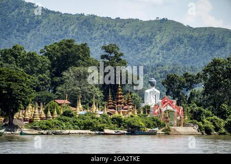 Blick von hinten auf einen riesigen Buddha neben Pagoden und goldenen Stupas auf der Insel Shwe Paw und Boote, die entlang des Ayeyarwady (Irrawaddy) Flusses anhegen Stockfoto