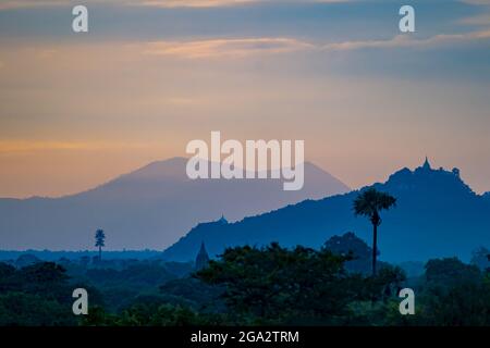 Silhouette der Berge und Pagoden mit dem ersten Licht des Sonnenaufgangs über der Landschaft der Ebene von Bagan im Morgengrauen; Bagan, Mandalay, Myanmar (Burma) Stockfoto