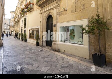 Straßenszene mit Menschen, die an Schaufenstern und den Kalksteingebäuden in der Altstadt von Lecce vorbeigehen; Lecce, Apulien, Italien Stockfoto