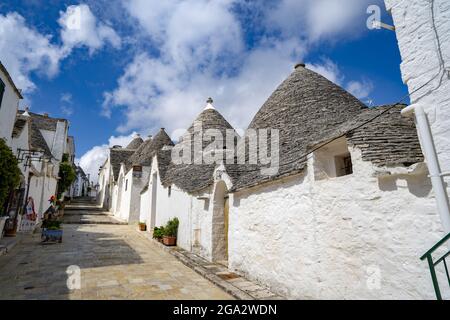 Straßenszene mit einer Reihe von traditionellen Apulischen runden Steinhäusern Trulli in der Stadt Alberobello; Alberobello, Apulien, Italien Stockfoto