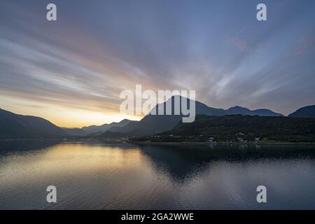 Mitternachtssonne mit einem dramatischen Himmel in der Dämmerung, von einem Kreuzschiff in den Fjorden gesehen; Westfjorde, Norwegen Stockfoto