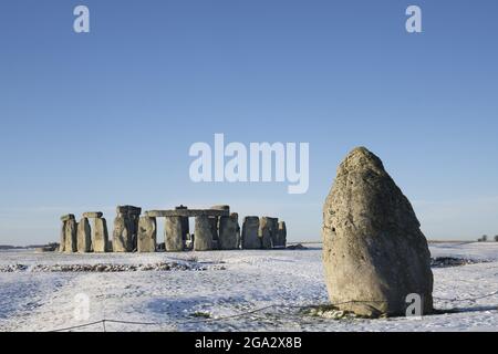 Stonehenge, definiert durch frühmorgendlichen Schnee mit einem blauen Himmel und dem Heel Stone rechts vom Steinkreis; Wiltshire, England, Vereinigtes Königreich Stockfoto