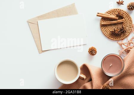 Herbstkomposition. Femininer Schreibtisch mit Brief, unbeschriftete Papierkarte, brauner Schal auf weißem Hintergrund. Flach liegend, Draufsicht. Nordisch, Hygge, gemütliches Zuhause c Stockfoto